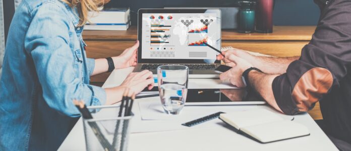 Cross-Channel-Marketing Business meeting. Teamwork. Businessman and businesswoman sitting at table in front of laptop and working. Man shows pencil on computer screen.Graphs,charts and diagrams on PC screen.Online education.