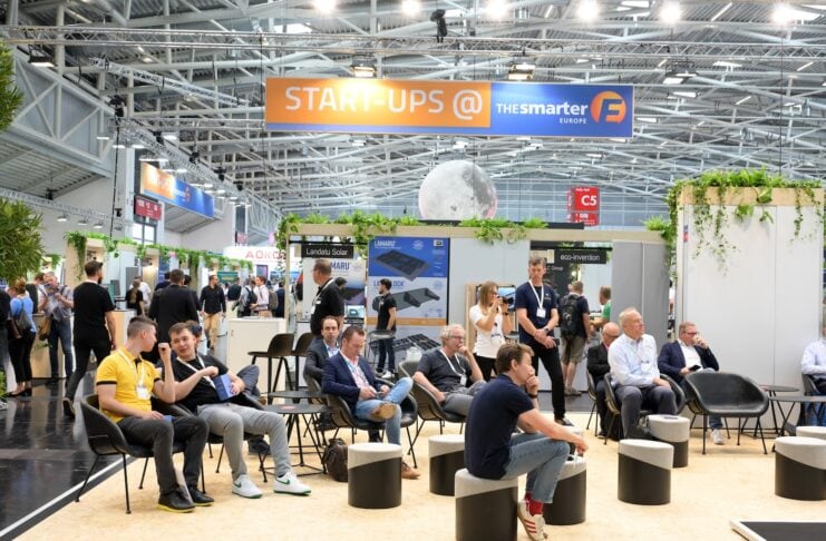 EM-POWER-EUROPE Ein paar Messebesucher bei einem Vortrag sitzend auf Würfeln und Stühlen im Hintergurnd findet man ein paar Stände auf der Messe