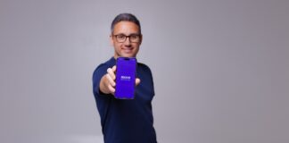 MovePayment Echtzeit-Überweisung Gründer Mohamed Seddiki mit Handy in der Hand vor einen Grauen Wand!
