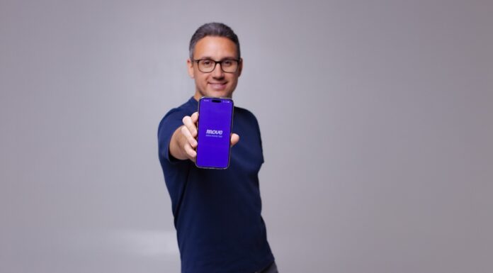 MovePayment Echtzeit-Überweisung Gründer Mohamed Seddiki mit Handy in der Hand vor einen Grauen Wand!