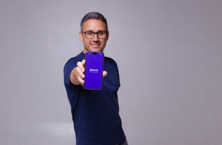 MovePayment Echtzeit-Überweisung Gründer Mohamed Seddiki mit Handy in der Hand vor einen Grauen Wand!