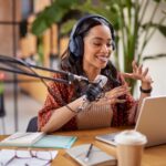 Podcast 2025 starten: Video Podcast & KI clever nutzen Podcast 2025 starten: Video Podcast & KI clever nutzen Junge Frau sitzt am Tisch und nimmt einen Podcast auf vor Ihr stehet ein Lapptop und ein Großes Podcast Mikrophon