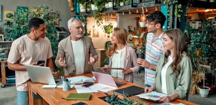 Startup Gründen 2025 Gründer Team die sich an einem Tisch im Office beraten!Gruppe junger Geschäftsleute und Seniorchef arbeiten zusammen mit Laptop, Tablet, Smartphone, Notebook und Grafiken. Erfolgreiches Team im Coworking