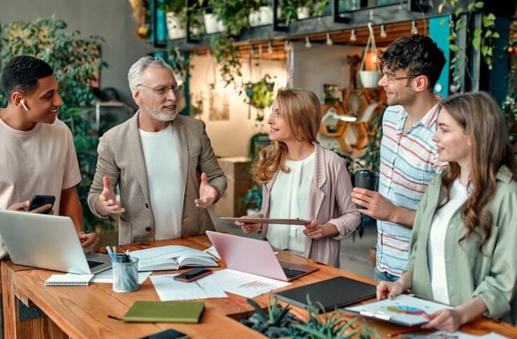 Startup Gründen 2025 Gründer Team die sich an einem Tisch im Office beraten!Gruppe junger Geschäftsleute und Seniorchef arbeiten zusammen mit Laptop, Tablet, Smartphone, Notebook und Grafiken. Erfolgreiches Team im Coworking
